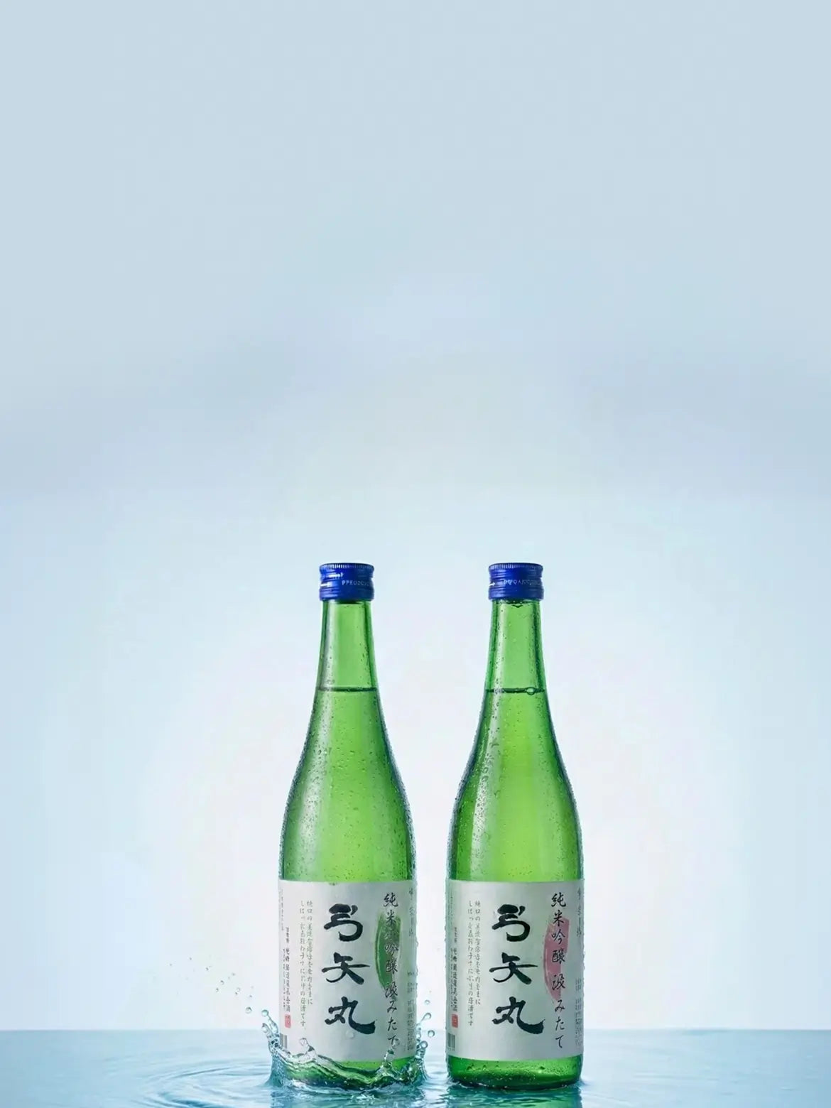Two green sake bottles with labels on a blue water background
