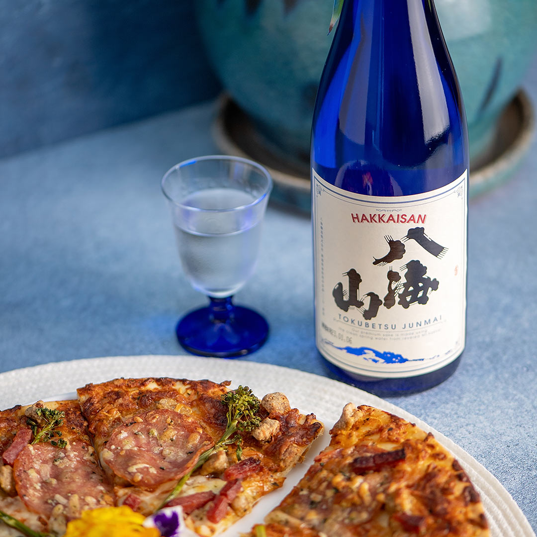 Hakkaisan “Tokubetsu Junmai”, with a clear glass cup with blue mini stem, served with pizza