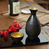 “Mino no Takumi” Black Tokkuri With Blue Drip Glaze and Gold Interior, on a table Thumbnail